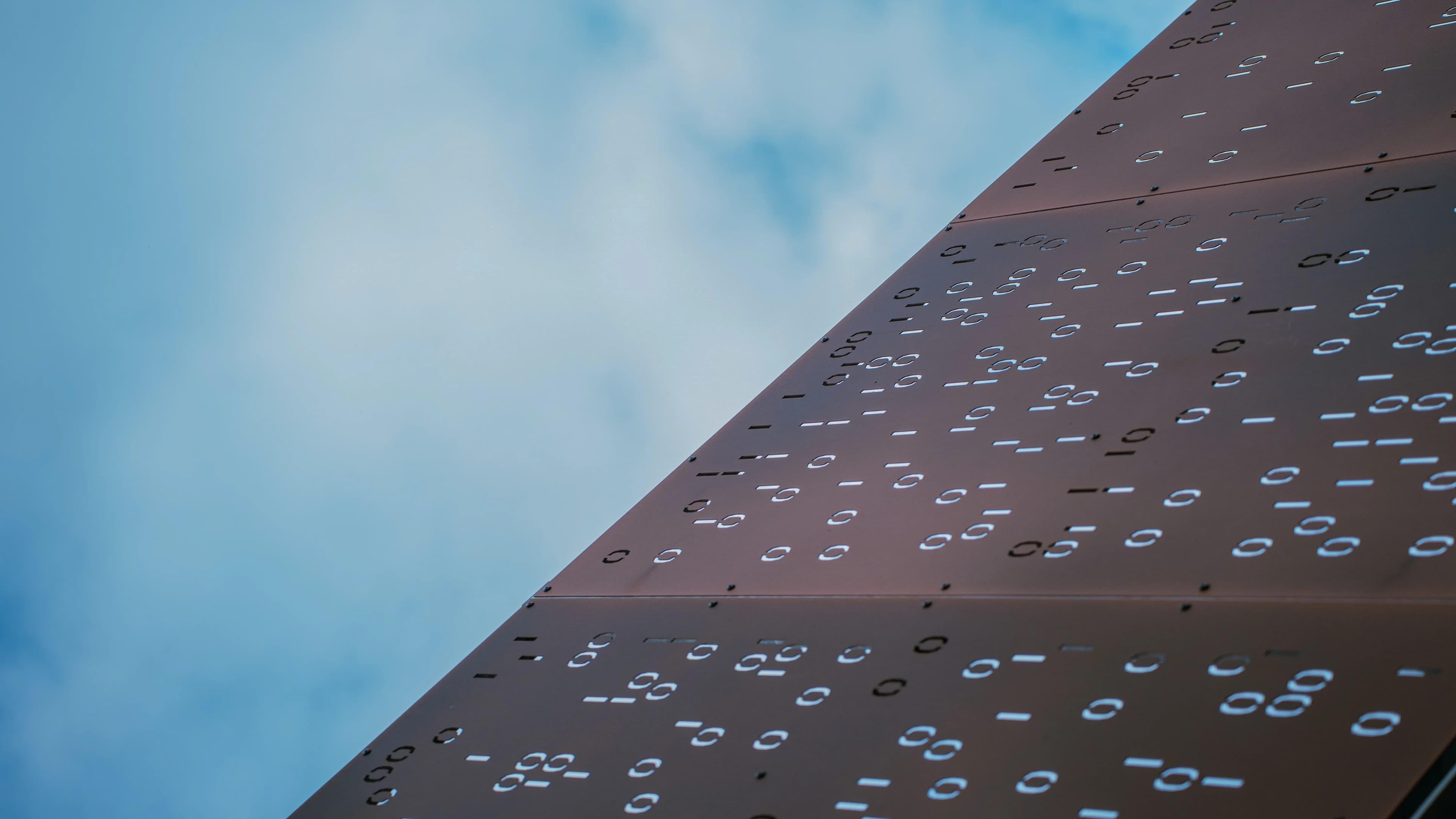 Vue en contre-plongée du toit métallique du data center Eclairion avec motifs code binaire sur fond de ciel